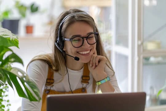 A smiling person working from home with a laptop and headset